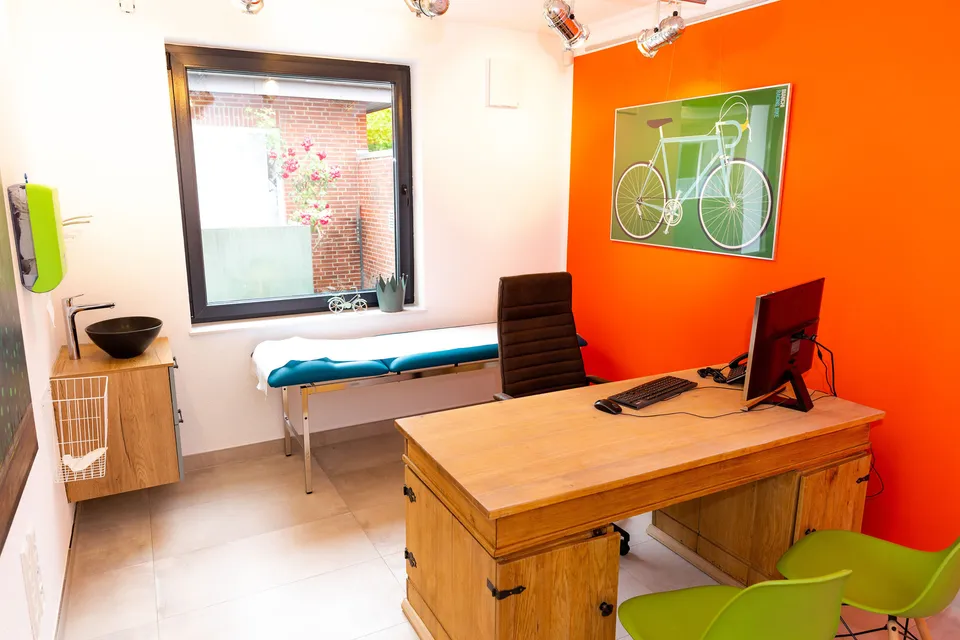 Behandlungszimmer mit orangefarbener Wand und Fahrradbild.